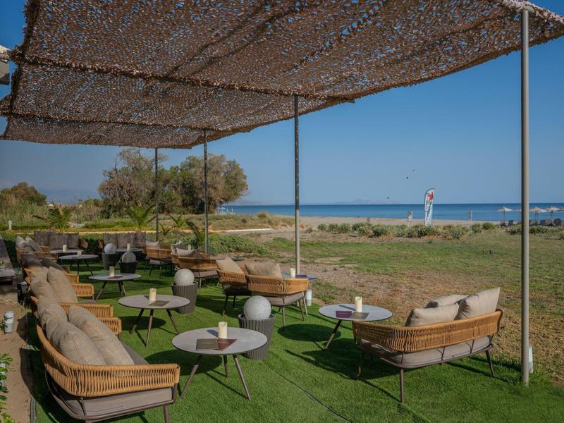 Áreas exteriores acogedoras con sillones y mesas bajo sombra cerca de la vista al mar.