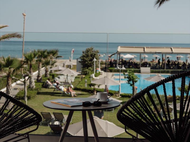 Balcón con sillas y mesa con vista al mar, piscina y jardín en un hotel.