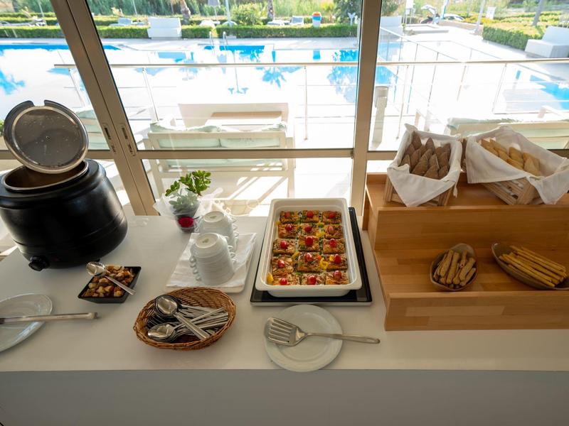 Buffet del hotel con varios platos junto a ventana grande con vista a la piscina.