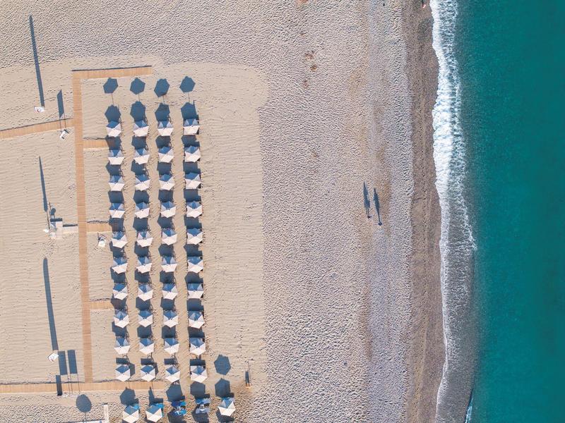 Vista aérea de una playa con filas de sombrillas, arena y mar azul.