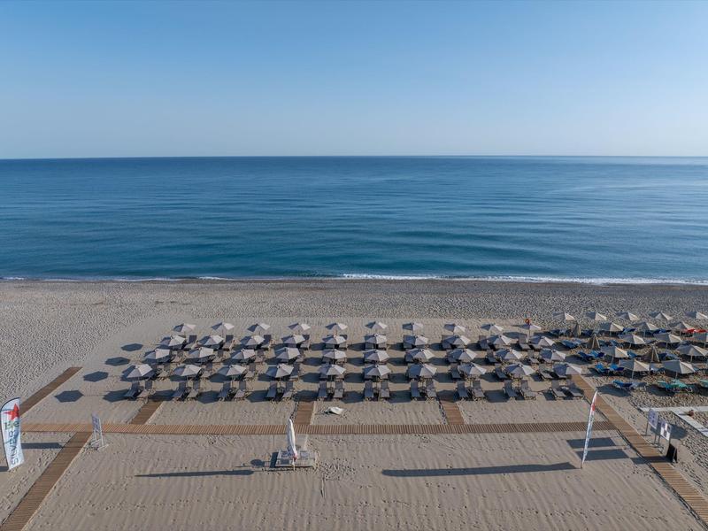 Playa con muchas sombrillas y tumbonas frente al mar azul tranquilo bajo un cielo despejado.