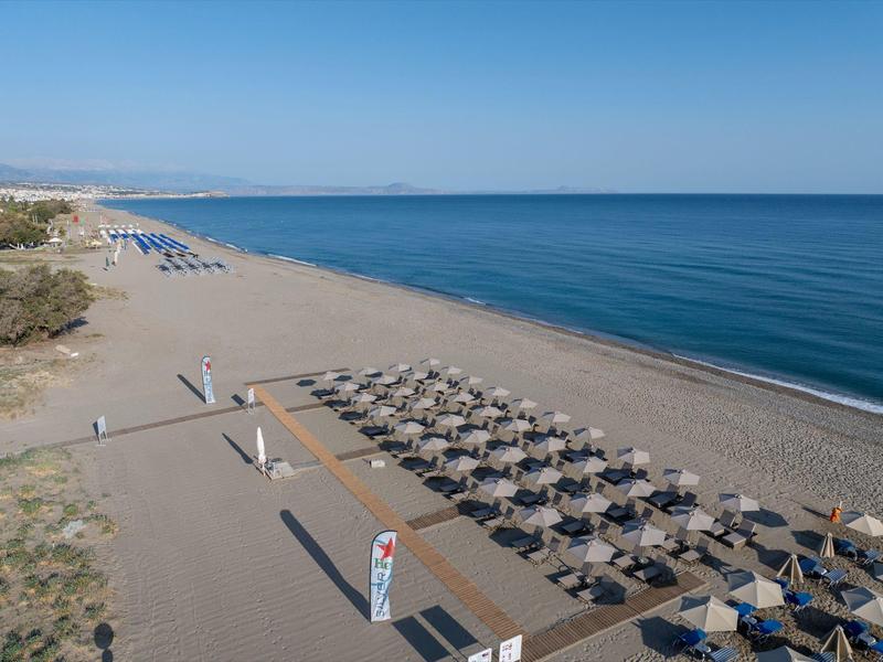 Amplia playa de arena con filas de sombrillas y tumbonas junto al mar tranquilo.