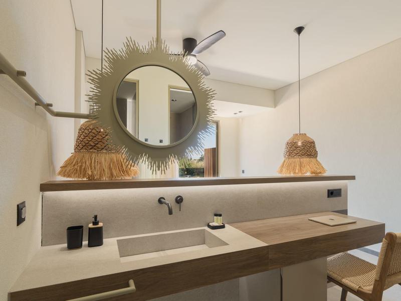 Lavabo moderno de hotel con espejo redondo y lámparas colgantes elegantes en un espacio iluminado.