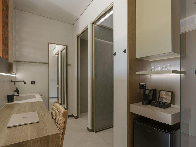 Área de trabajo moderna en hotel con escritorio de madera, silla y vista al baño con ducha de cristal.