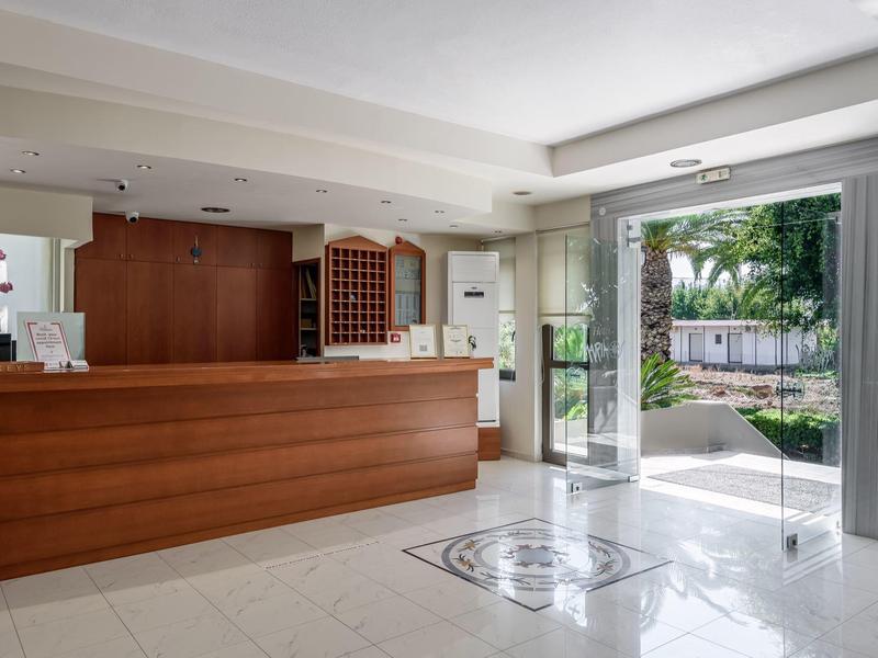 Recepción de hotel luminosa con mostrador de madera, área de espera y ventanales al jardín exterior.