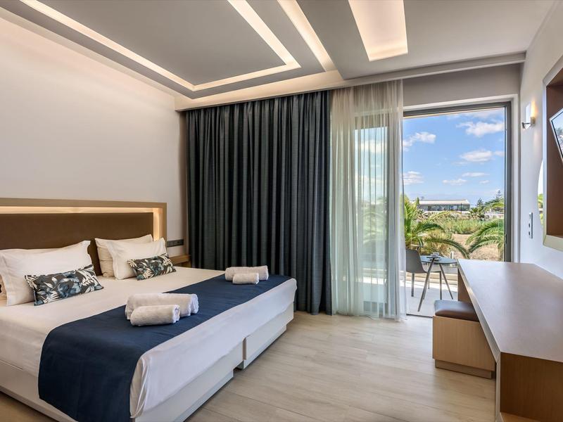 Habitación de hotel moderna con cama doble, cortinas oscuras y balcón con vista a la piscina y el paisaje.