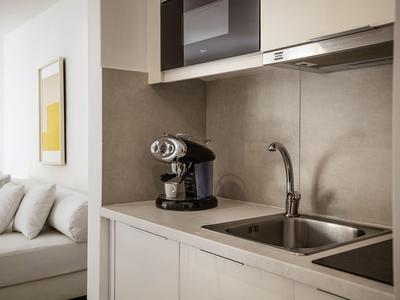 Moderne Küchenzeile mit Spüle, Kaffeemaschine und angrenzendem Wohnzimmer mit Sofa.