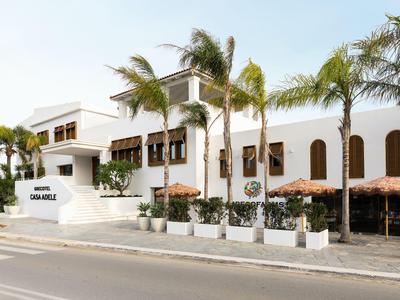 Modernes, weißes Hotelgebäude mit Palmen und Straßenseite im Vordergrund.