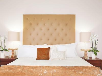 Cama cómoda con cabecero acolchado marrón, mesitas con lámparas y orquídeas.