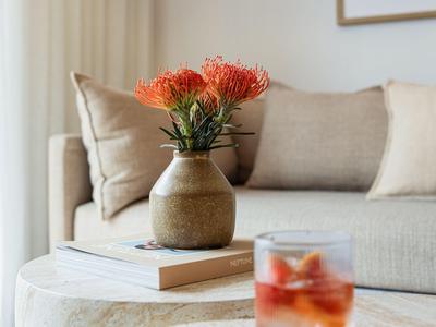 Vaas met oranje bloemen op een salontafel voor een beige bank in een lichte kamer.