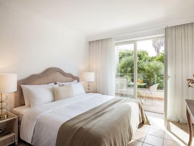 Helles Schlafzimmer mit großem Bett, zwei Nachttischen und Blick auf eine Terrasse mit Garten.