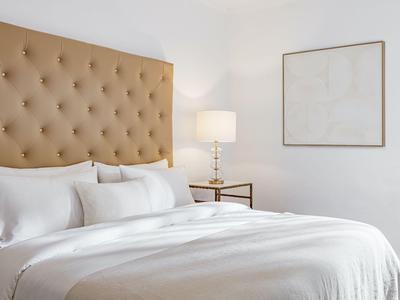 Helles Schlafzimmer mit großem Bett, gepolstertem Kopfteil und Nachttischlampe.