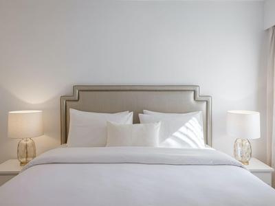 Modernes Doppelbett mit weißen Kissen und Bettwäsche, flankiert von zwei Nachttischlampen.