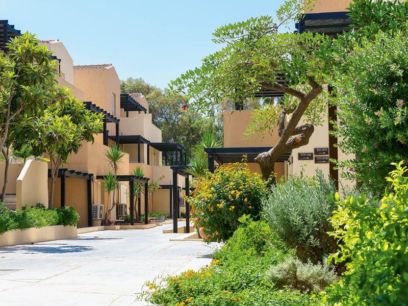 Patio interior de un hotel con áreas verdes, árboles y edificios modernos en un día soleado