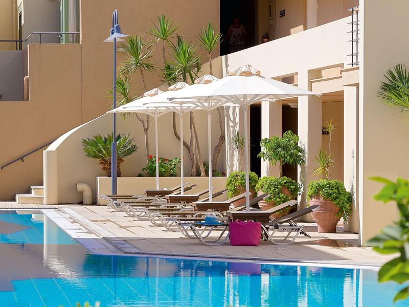 Piscina moderna de hotel con tumbonas y sombrillas junto a una terraza con plantas.