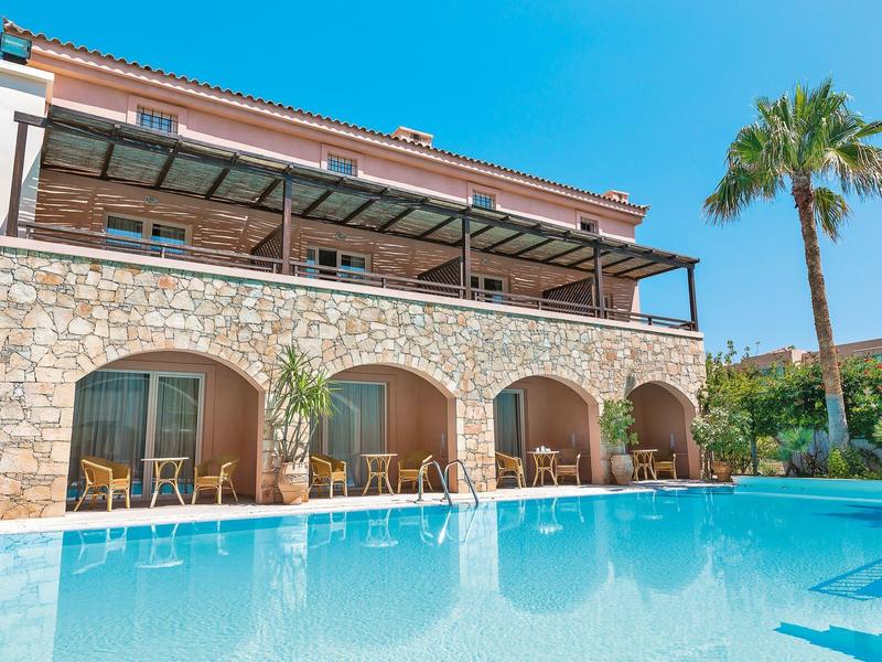Hotel con piscina, muro de piedra y terraza con mesas y sillas bajo cielo azul