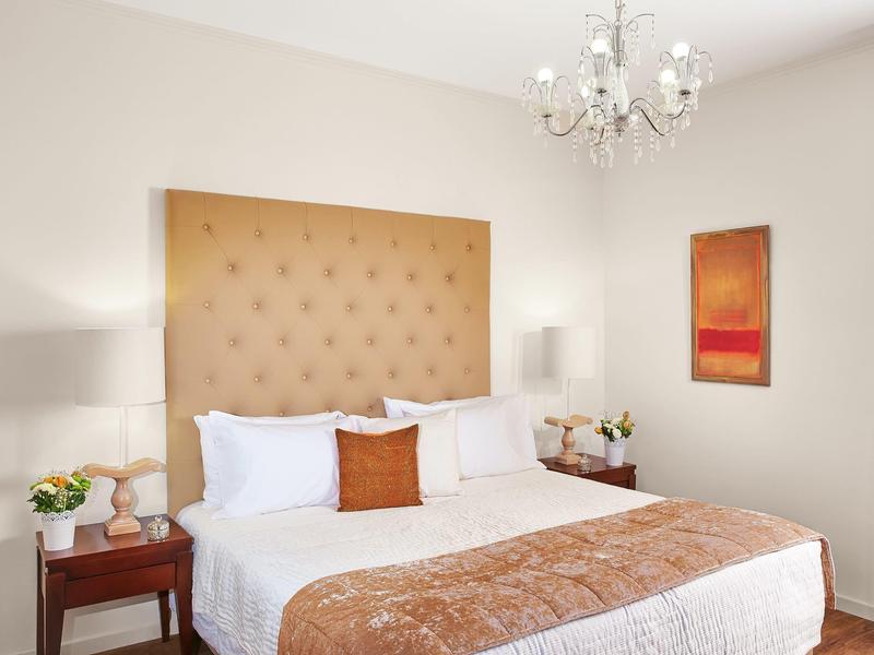 Habitación de hotel luminosa con cama grande, cabecero beige y araña de luces.