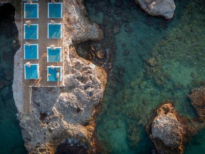 Drohnenaufnahme von Pools auf Felsen neben klarem blauem Meerwasser.