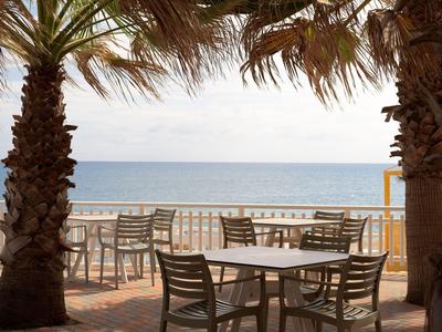 Leere Stühle und Tische zwischen zwei Palmen mit Blick auf das Meer und den Himmel.