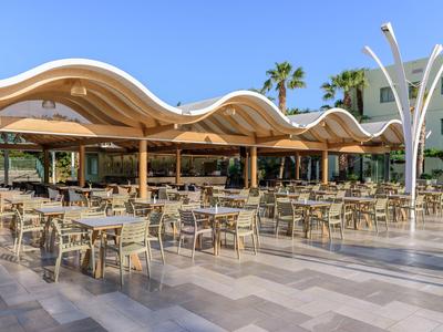 Freiluftrestaurant mit Wellendach und vielen Tischen und Stühlen bei sonnigem Wetter.