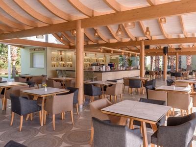 Ristorante moderno con mobili in legno e sedie in tessuto sotto un tetto di stoffa bianca.