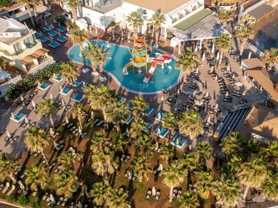 Vista aerea di un resort con piscina, ombrelloni e palme vicino alla spiaggia.