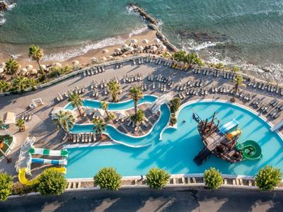 Vista aerea di una grande piscina all'aperto con forme arrotondate, palme e una nave pirata, circondata da lettini vicino al mare.