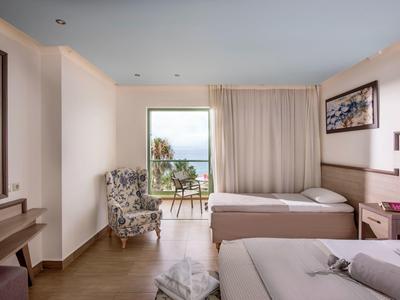 Camera d'hotel luminosa con due letti e balcone con vista mare.