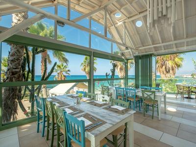 Offener Speiseraum mit Blick auf das Meer, hell und luftig mit Tischen und blauen Stühlen.