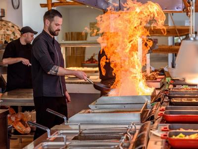 Cuoco crea grandi fiamme sopra il fornello in cucina di ristorante.