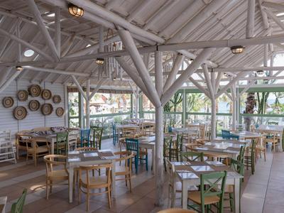 Helle, offene Restaurantfläche mit gemischten Holztischen und Stühlen unter einem weißen Fachwerkdach.