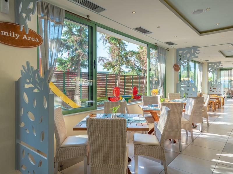 Zona pranzo luminosa con sedie in vimini, decorazioni sul tavolo e vista su un parco giochi esterno.