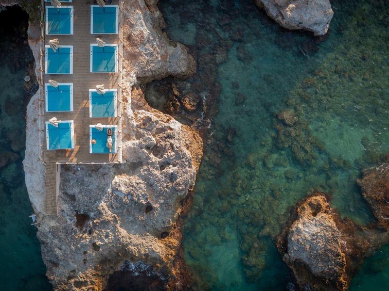 Veduta aerea di una roccia con diverse piccole piscine vicino al mare turchese limpido.