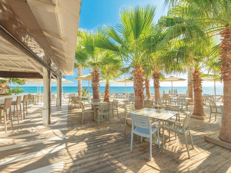 Ristorante sulla spiaggia con tavoli e sedie sotto le palme con vista sul mare blu.