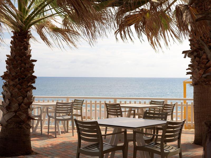 Caffè sulla spiaggia con tavoli e sedie tra palme con vista sul mare.