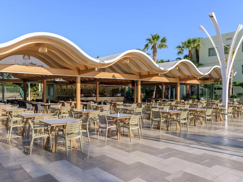 Ampia terrazza con molti tavoli e sedie sotto una tenda ondulata in una giornata serena.
