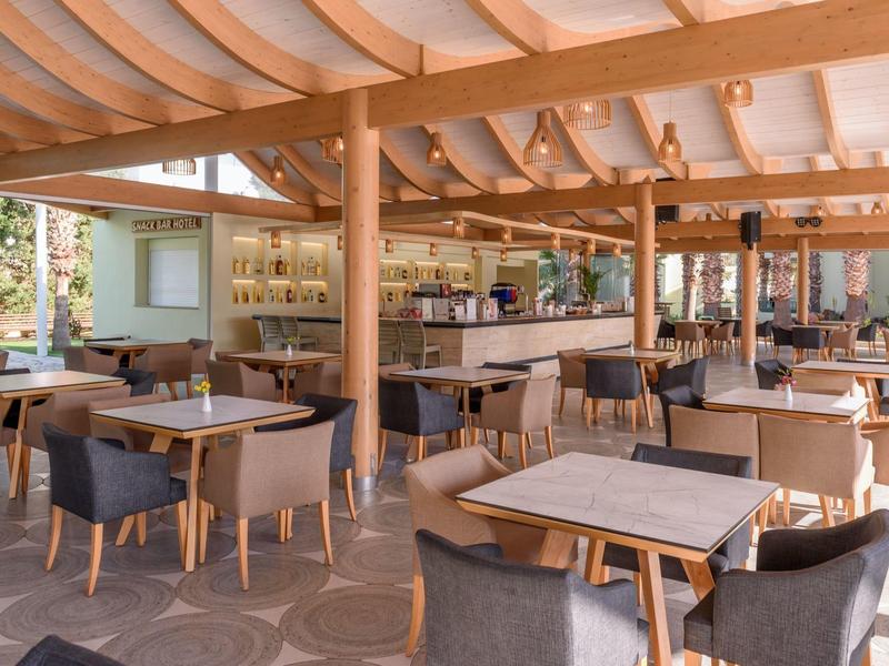 Ristorante moderno con mobili in legno e sedie in tessuto sotto un tetto di stoffa bianca.