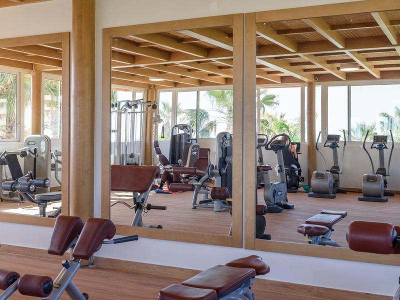 Palestra luminosa con soffitto a travi di legno, parete a specchio e varie attrezzature.