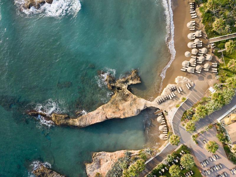 Vista aerea di un resort sulla spiaggia con spiaggia sabbiosa, rocce e lettini vicino al mare.