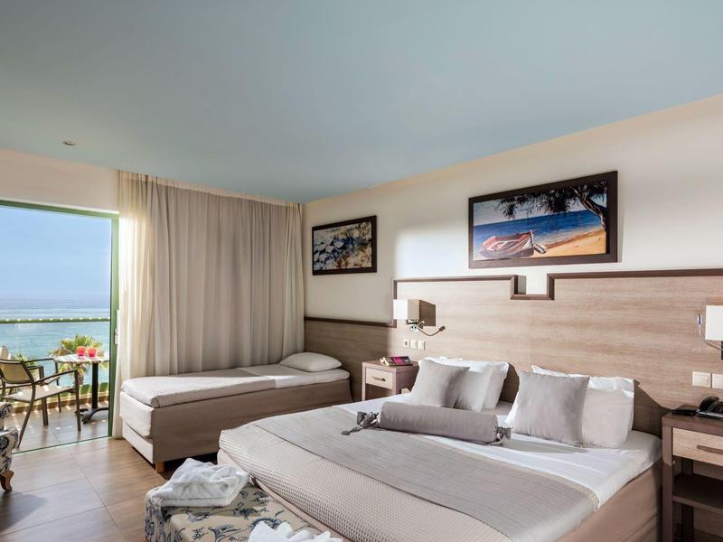 Camera d'hotel con due letti matrimoniali, balcone con vista mare e arredamento moderno.