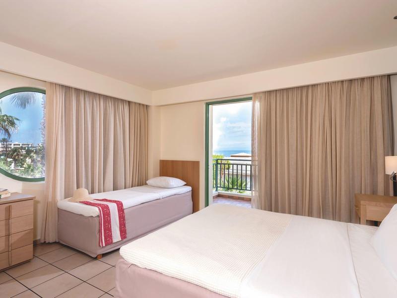 Camera d'hotel con due letti, scrivania e finestra rotonda con vista sulle palme.