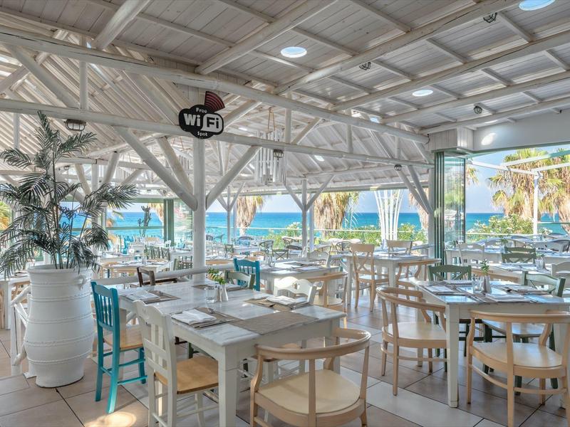 Bar sulla spiaggia luminosa e aperta con tavoli bianchi, sedie e vista sul mare.