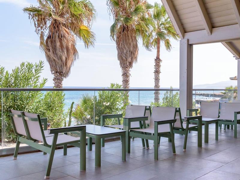 Balcone con zona salotto moderna, ringhiera in vetro e vista su palme e mare.