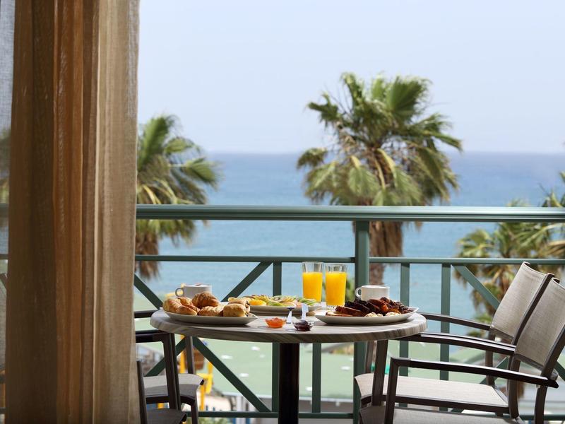 Tavolo sul balcone con colazione e vista sul mare, palme sullo sfondo.