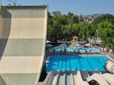 Wasserrutsche beim Hotelpool mit Liegestühlen und Bäumen im Hintergrund.
