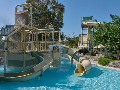 Wasserrutschpark mit mehreren Rutschen, Bäumen und einem klaren blauen Pool.