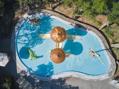 Außenpool mit zwei Sonnenschirmen in einem von Bäumen umgebenen Hotelgarten