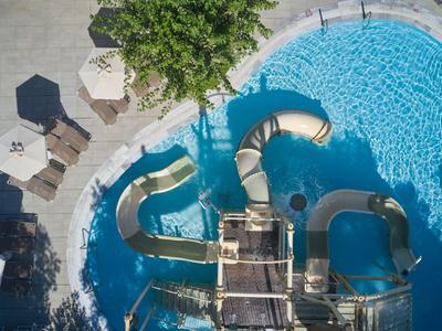 Vogelperspektive auf Pool mit geschwungenen Wasserrutschen und Liegestühlen im Schatten.