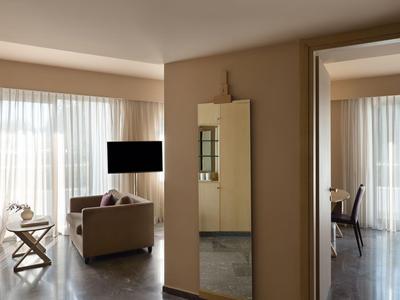 Habitación de hotel luminosa con sofá, TV en la pared y gran espejo cerca de la entrada.