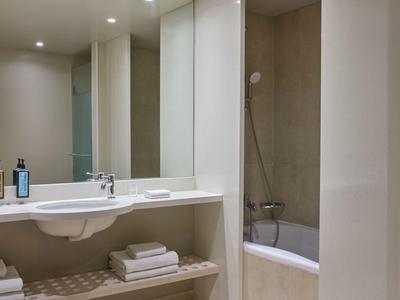 Baño moderno de hotel con lavabo blanco, bañera y toallas en una estantería.